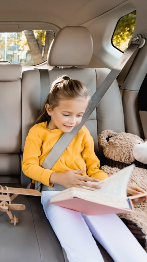 Smiling kids with smartphone, toys and book sitting in a car