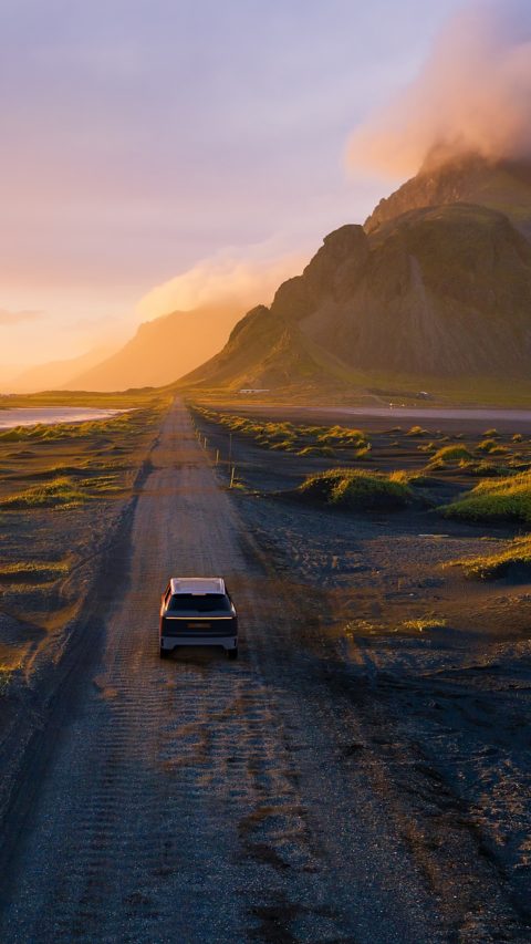 Gravel road at a golden Sunset with Vestrahorn mountain in the background and a car driving the road in Iceland