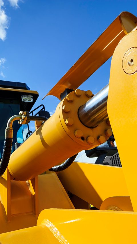 Bulldozer, huge yellow powerful construction machine with big scoop, focused on hydraulic piston arm, heavy industry, blue sky and white clouds on background