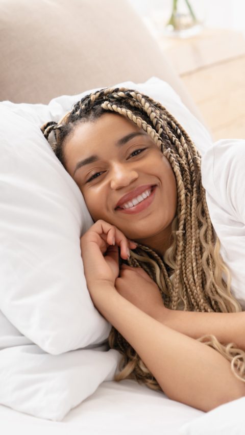 Image of an african-american girl relaxing in her bed. Serene calm afro woman sleeping in comfortable bed lying on soft pillow orthopedic mattress. Side view