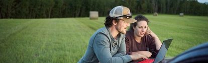 Young farmer couple looking at a laptop on pick-up truck hood while working on a farm