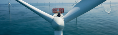 Rotorblätter eine Windturbine in Nahaufnahme, im Hintegrund stehen weitere Turbinen im ruhigen Meer.