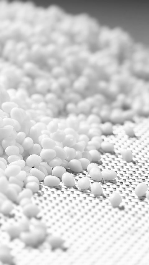 Closeup of a granule of white plastic polymer in a laboratory against gray background.