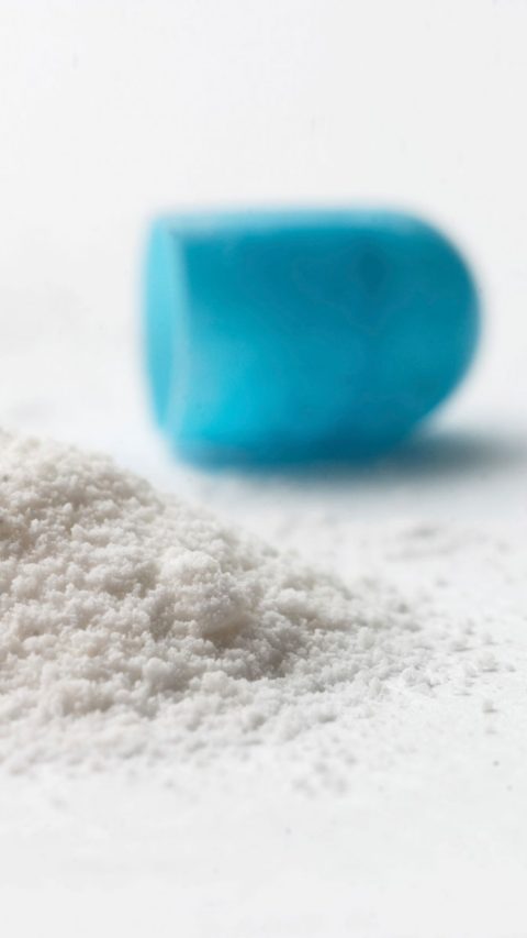 Close up of a pill with blue cap with small mountain of white powder 