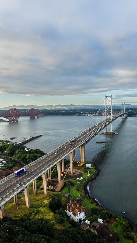 The new Queensferry Crossing bridge (on the right) under construction over the Firth of Forth with the older Forth Road bridge (on the left) and with the iconic Forth Rail Bridge in the far left.