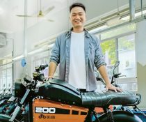 Son Nguyen standing behind a moped in a store. His hands are placed on the bike.