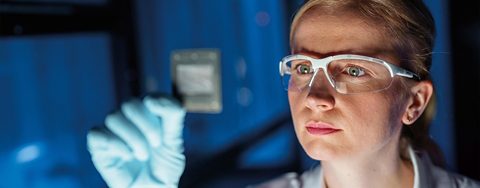 Woman in safety goggles inspecting item in a lab
