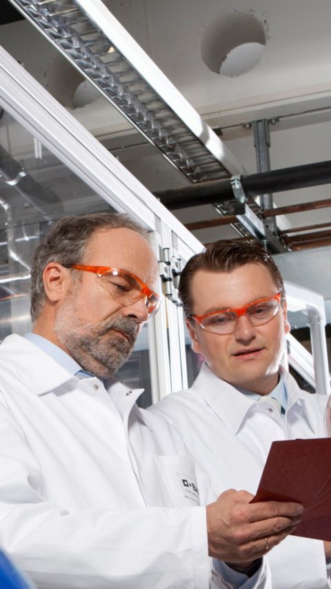 Two scientist wear red safety goggles analyzing chemical holding cue cards 