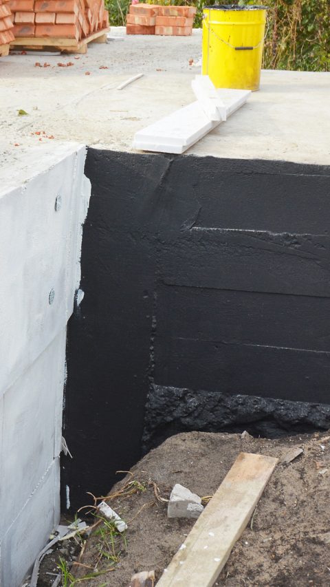 Waterproofing house foundation with  bitumen and styrofoam rigid foam insulation against water leaking.