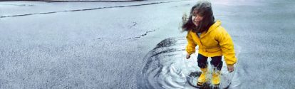 Girl (3-5) jumping in puddle wearing rain gear